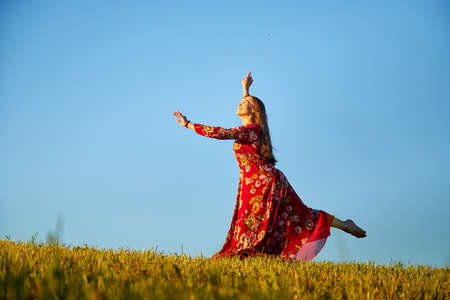 Beautiful woman or girl with magnificent figure and plastic movements walking and dancing in green field with trimmed grass in the setting sun during sunset with warm yellow lightの写真素材