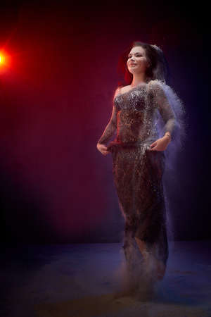 Girl in black dress posing in dark studo during photoshoot with flour or dust and light. Dangerous...