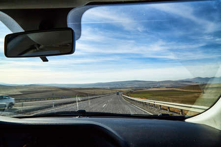 View from car window on the road and strange landscape with a valley, mountains and blue sky with clouds. Landscape through windscreen in Cappadocia at Turkeyのeditorial素材