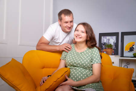 Cute couple including a pregnant woman and a caring man in the living room together. Beautiful...