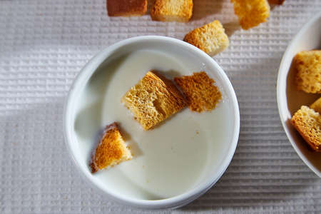 Square toasted pieces of homemade delicious rusk, hardtack, Dryasdust, zwieback and plate of milk on a white tableclothの写真素材