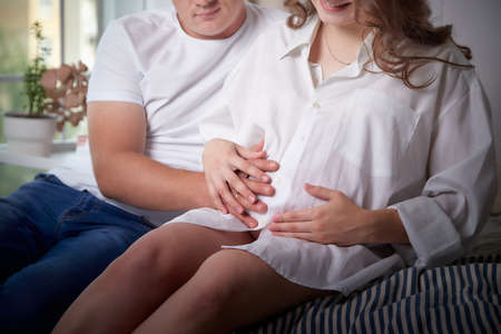 Cute couple including a pregnant woman and a caring man together on the bed on the bed with white...