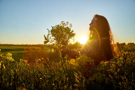 Beautiful woman with long hair in red dress holding bouquet of yellow flowers and enjoying summer...
