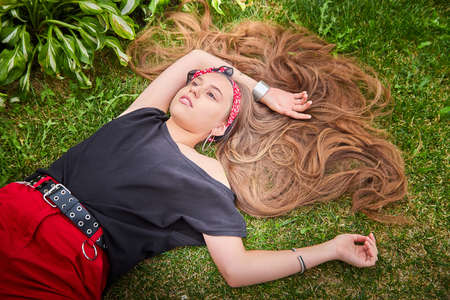 Young girl with long hair lying on the lawn with green grass in a day. Teenager model posing on natureの写真素材