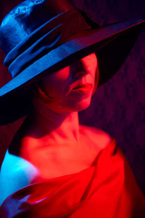 Portrait of ugle middle-aged woman with hat and red dress. Ugly model looking as lady posing in studioの写真素材