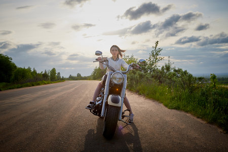 Attractive brunette motorcyclist with motorcycle in a summer evening during sunset. Adventure and travel conceptの写真素材