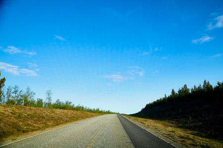 View from car windscreen with stripe relief to highway, tundra and blue sky in norht region at a...