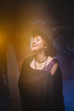 Slim witch in maroon dress and black hat in room decorated for Halloweenの写真素材