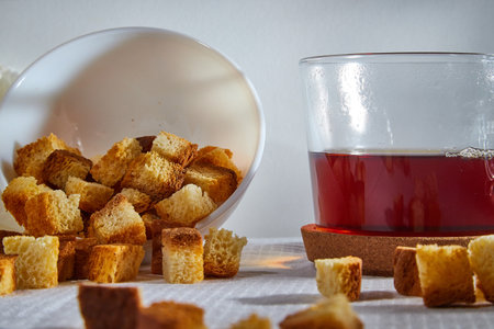 Square toasted pieces of homemade delicious rusk, hardtack, Dryasdust, zwieback on a plate and black tee in a cap on a white tableclothの写真素材
