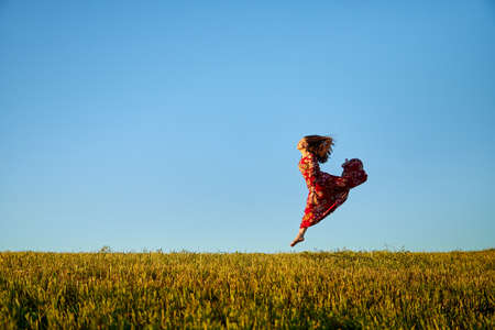 Beautiful woman or girl with magnificent figure and plastic movements walking and dancing in green field with trimmed grass in the setting sun during sunset with warm yellow lightの写真素材