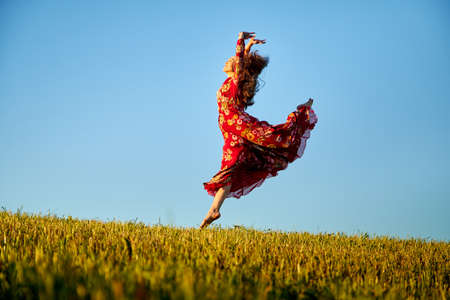 Beautiful woman or girl with magnificent figure and plastic movements walking and dancing in green field with trimmed grass in the setting sun during sunset with warm yellow lightの写真素材