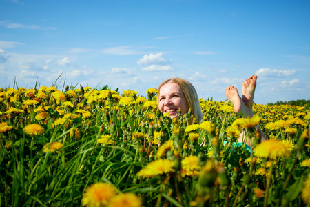 Pretty woman on a field with green grass and yellow dandelion flowers in a sunny day. Girl on nature with yellow flowers and blue skyの写真素材