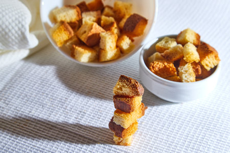 Square toasted pieces of homemade delicious rusk, hardtack, Dryasdust, zwieback stand in columns near white plate on a white tableclothの写真素材