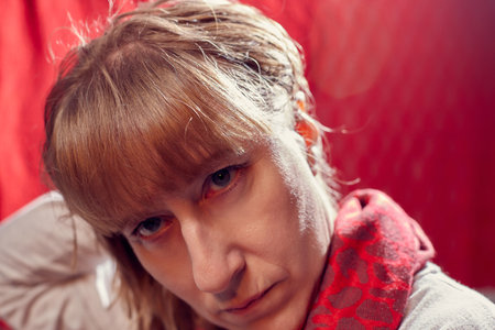 Portrait of serious sad middle-aged woman touching her hair on red background. Unprofessional female model in the Studio.の写真素材