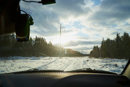 View of the winter snow road through the windshield of the car and the dark forest on the side of the roadの写真素材