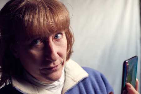 Portrait of a middle-aged woman with cell phone on a white background. Unprofessional female model doing selfie in the room or in the Studioの写真素材