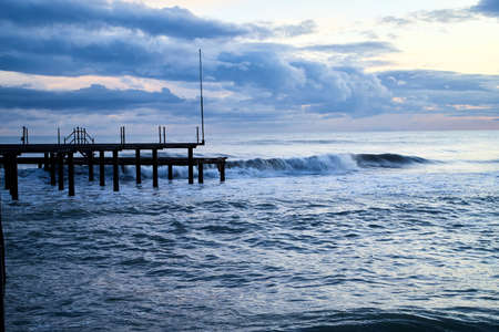 View from beach to water of sea, waves with white foam, pierce and sky with clouds in a nice eveningの写真素材