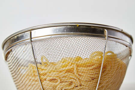 Long spaghetti in an iron colander on white background