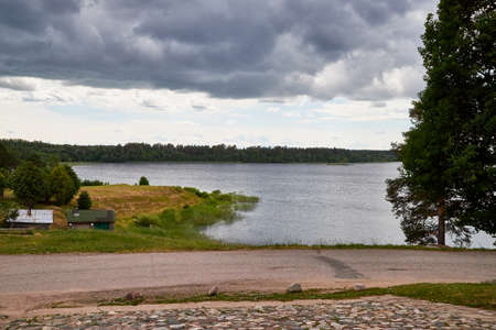 View of the lake water from the coast with trees and greenery, the horizon and blue sky with white...