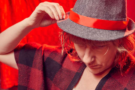 Portrait of serious sad middle-aged woman in hat on red background. Unprofessional female model in the Studioの写真素材