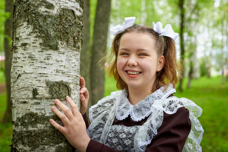Portrait of a young girl in an old school uniform of the USSR with a black dress and a white apron. Teenager in the Park among the greenery after graduating from school in Russia.の写真素材
