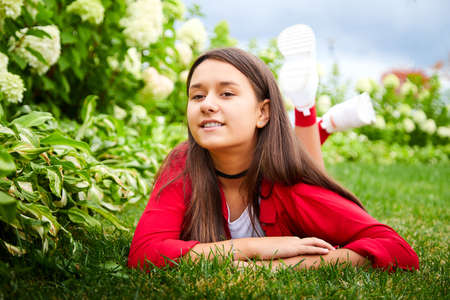 Young girl with long hair on the lawn with green grass and white flowers in a day. Teenager model posing on natureの写真素材