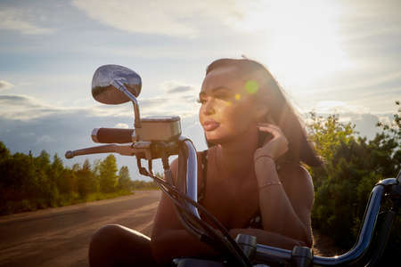 Attractive brunette motorcyclist with motorcycle in a summer evening during sunset. Adventure and travel conceptの写真素材