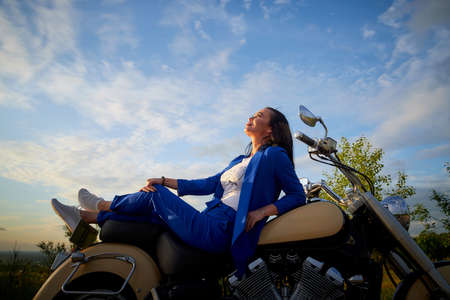 Attractive brunette motorcyclist with motorcycle in a summer evening during sunset. Adventure and travel conceptの写真素材