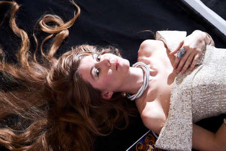 Young attractive girl with long blonde hair and beautiful dress posing lying on floor in studio on...
