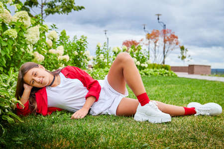 Young girl with long hair on the lawn with green grass and white flowers in a day. Teenager model posing on natureの写真素材