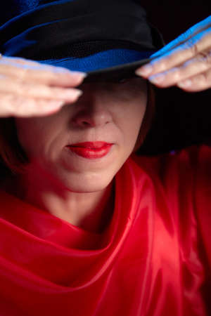 Portrait of ugle middle-aged woman with hat and red dress. Ugly model looking as lady posing in studioの写真素材