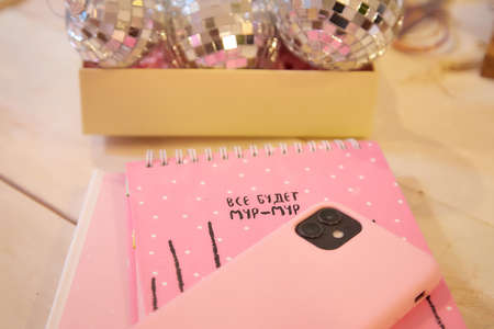 Pink notebook and wood table. Pink cell phone and Christmas ball on background