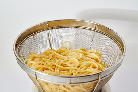 Long spaghetti in an iron colander on white background