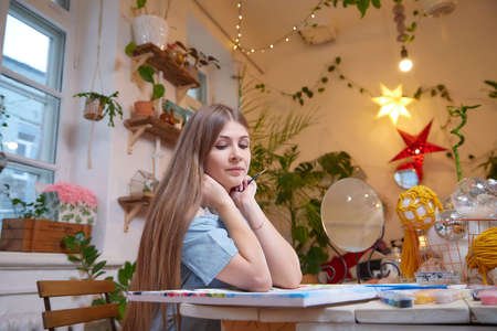 Kirov, Russia - December 17, 2020: Girl with long hair in room with a lot of things and picture. Portrait of a young artist drawing the picture in cozy houseの写真素材