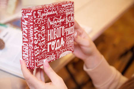 Red box with inscriptions in Russian Happy New Year in the hands of a girl in the room