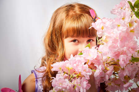 Young girl with blonde curly hair with a butterfly in the studio on a white background. Child posing during a photo shoot. The concept of spring, summer, childhood, happinessの写真素材