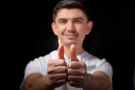 A young man who is a medical doctor in a white uniform poses against black background in the studio