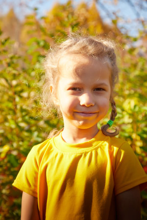 Portrait of young little girl with blonde curly hair in an autumn park on yellow and orange leaf...