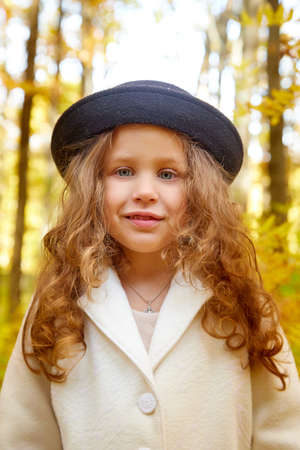 Portrait of young funny girl with blonde curly hair and in black hat in an autumn park on a yellow...