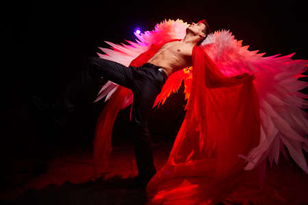 Handsome young athletic man with a bare torso who looks like an angel with white wings. Model dancer posing in a dark studio on black backgroundの写真素材