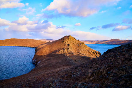 Beautiful natural view of the landscape with the shore with yellow grass, lake, and blue sky with white clouds on sunny autumn dayの写真素材