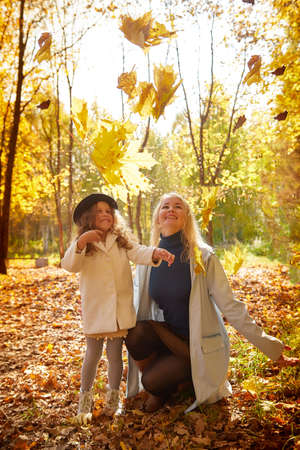 Mother and young little girl with blonde hair in an autumn park on a yellow and orange leaf background. Family walking in forestの写真素材