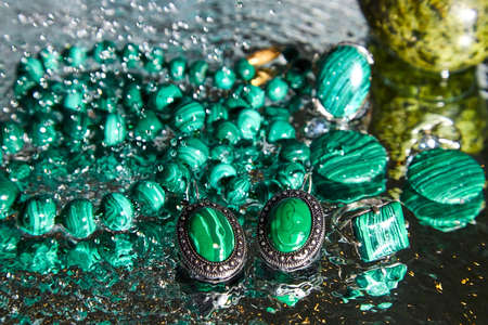 Jewelry from green malachite. Malachite beads in the studio on a glass surface with water