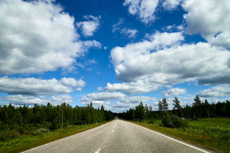 View from relief car windscreen on the blue sky with white clouds, grey asphalt road and landscape with forest and green teeses. Landscape through windowの写真素材