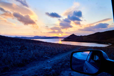 Car in beautiful natural view of the landscape with yellow shore, lake, and blue sky with white...