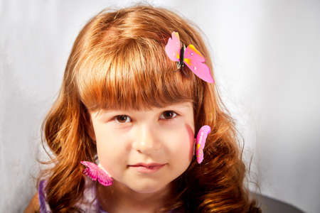 A young girl with blonde curly hair with a butterfly in the studio on a white background. Child...