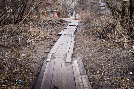 A wooden sidewalk goes through muddy wet countryside road. A path on wet clay.