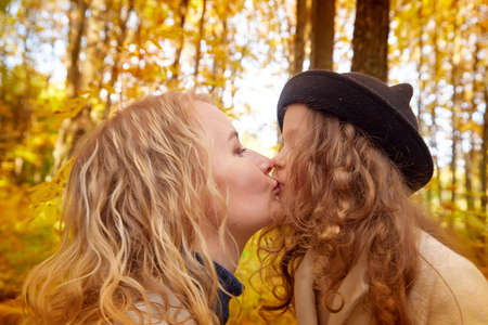 Mother and young little girl with blonde hair in an autumn park on a yellow and orange leaf background. Family walking in forestの写真素材