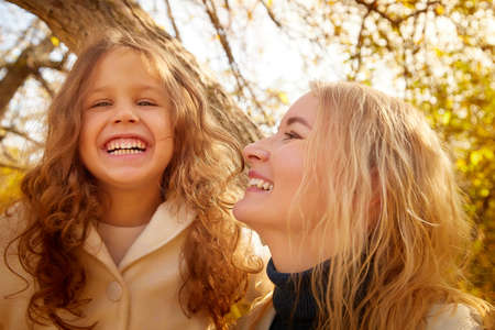 Mother and young little girl with blonde hair in an autumn park on a yellow and orange leaf background. Family walking in forestの写真素材