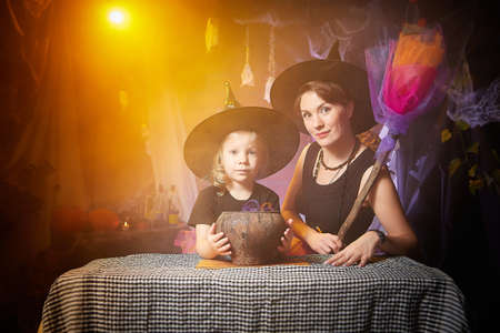 Beautiful brunette mother and cute little daughter looking as witches in special dresses and hats...